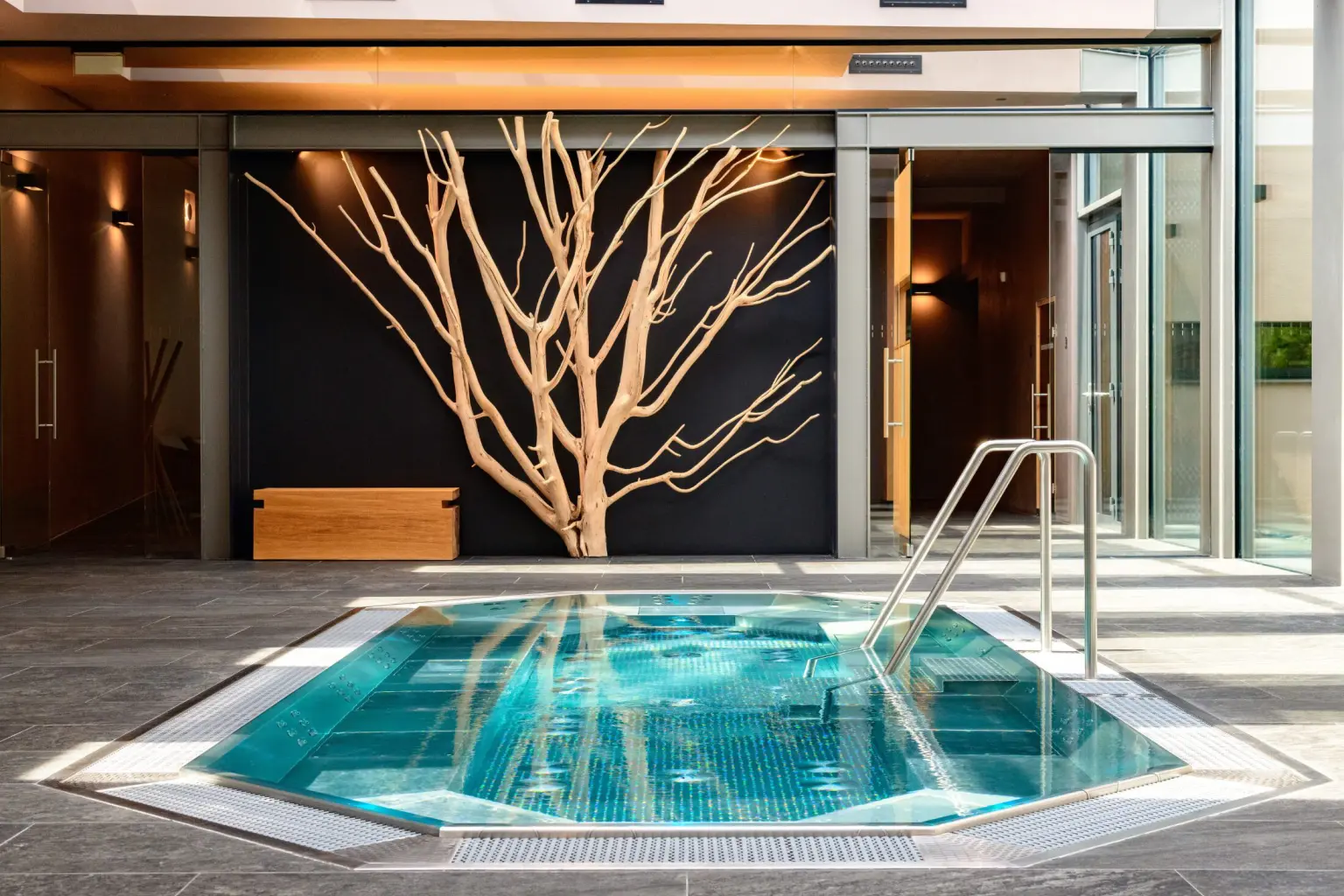Stainless steel spa pool with perimeter bench seating and hydrojets, set into an architectural stone floor